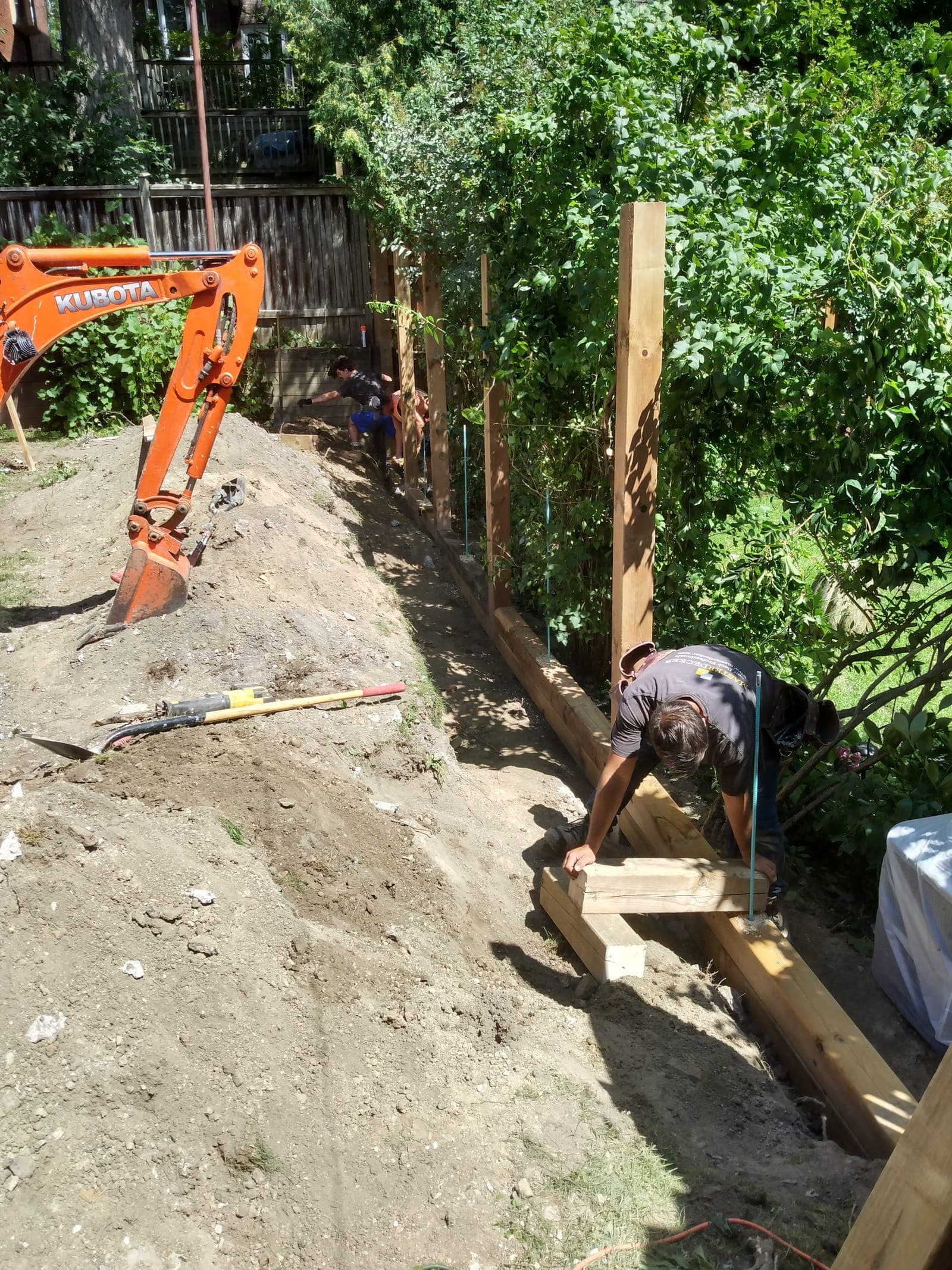 Timber retaining wall being installed with wooden posts along an excavated garden slope