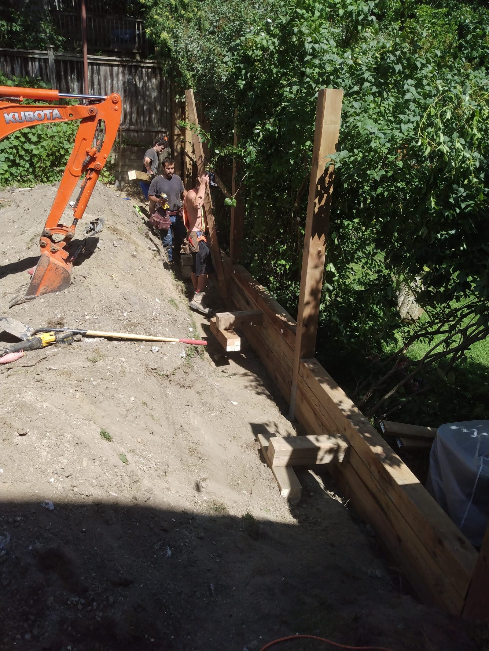 Timber retaining wall being built up with stacked pressure-treated courses along a backyard