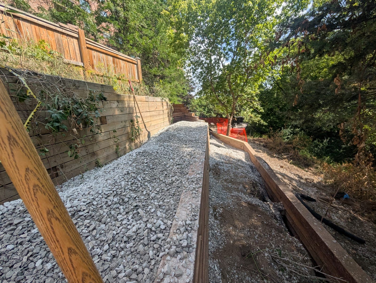 Timber retaining wall holding back a fenced slope above a gravel walkway in a backyard