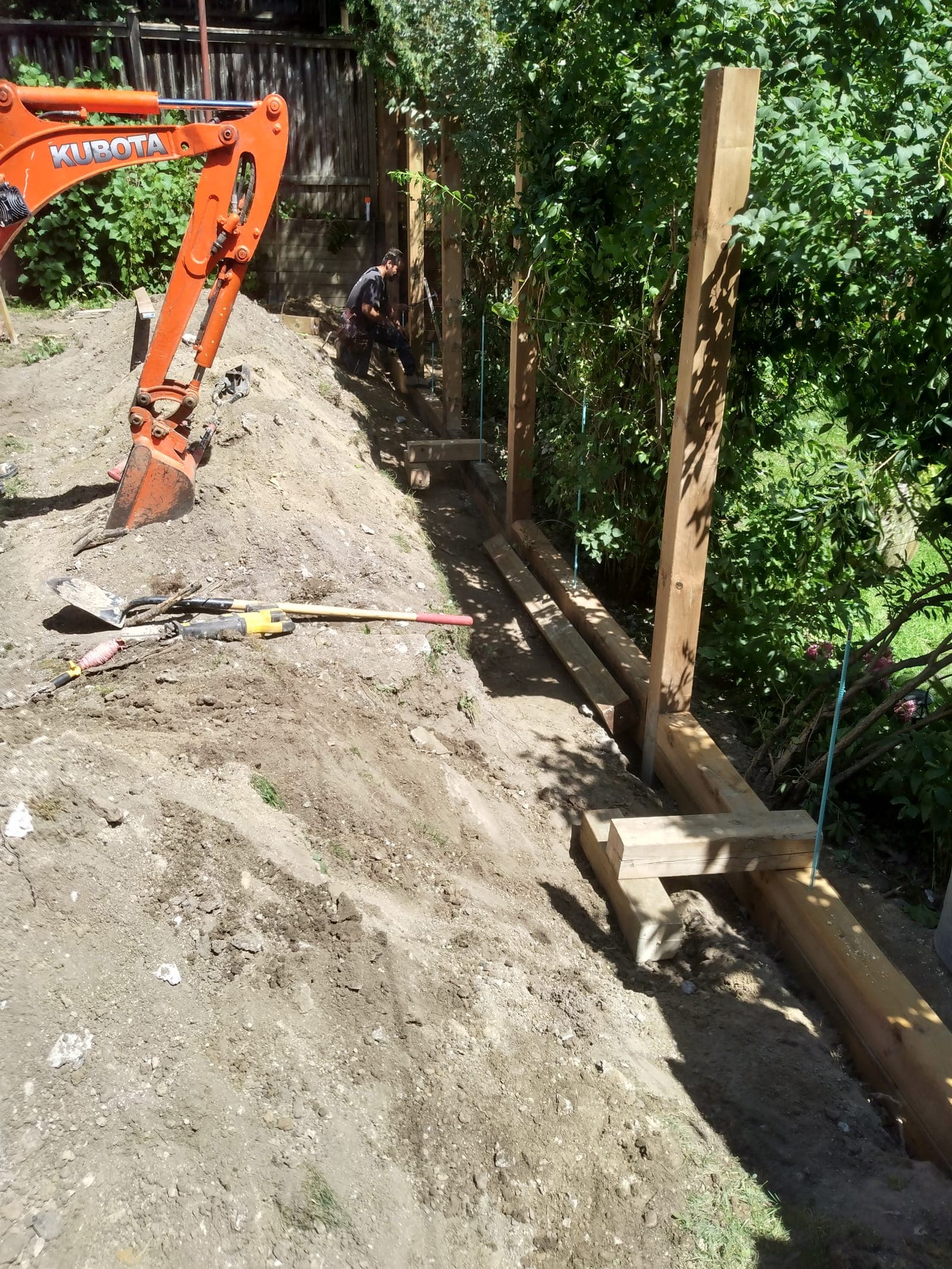 Timber retaining wall under construction with deadman tie-back anchors set into the slope