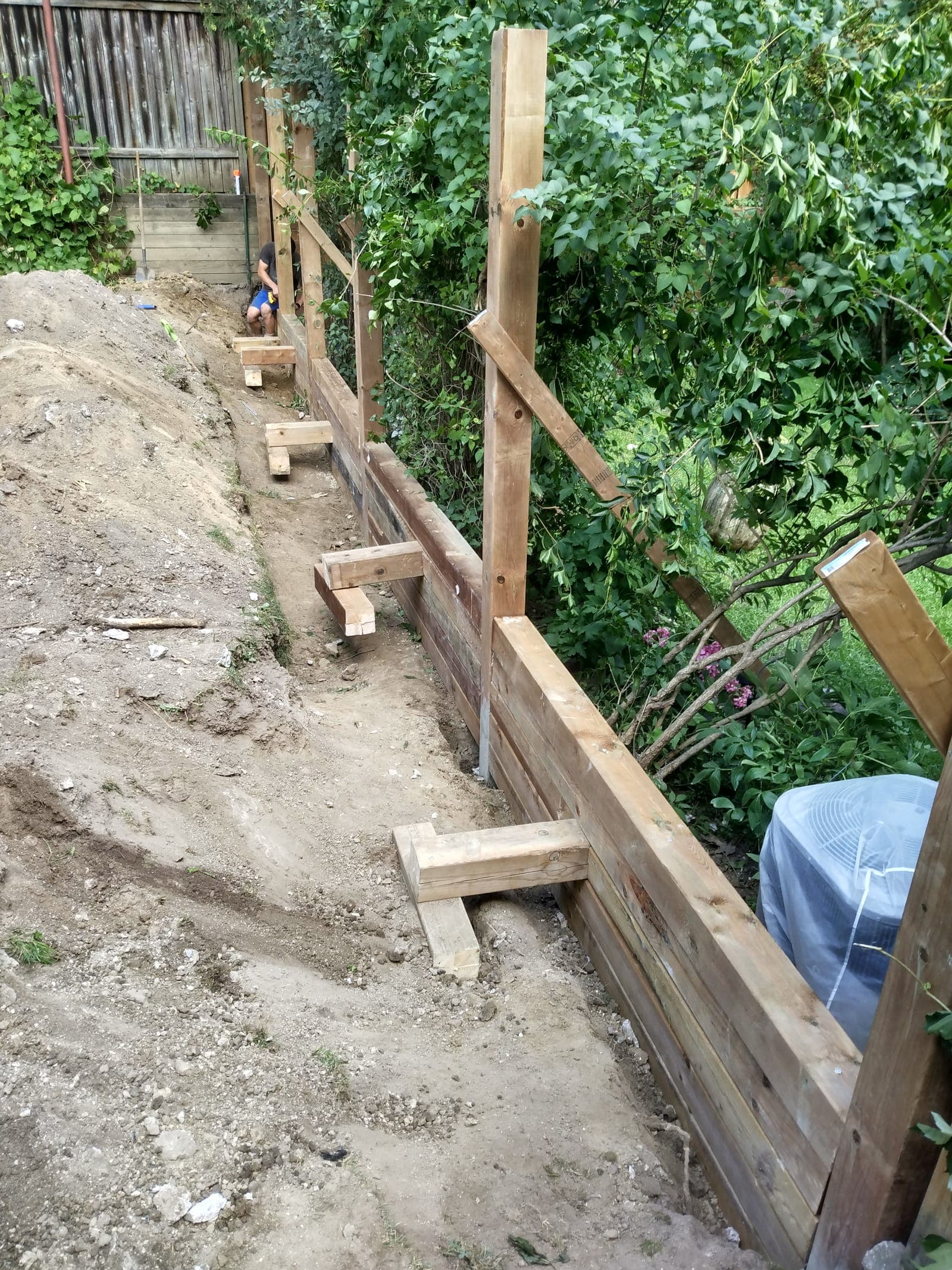 Timber retaining wall with visible deadman tie-back anchors along a landscaped slope