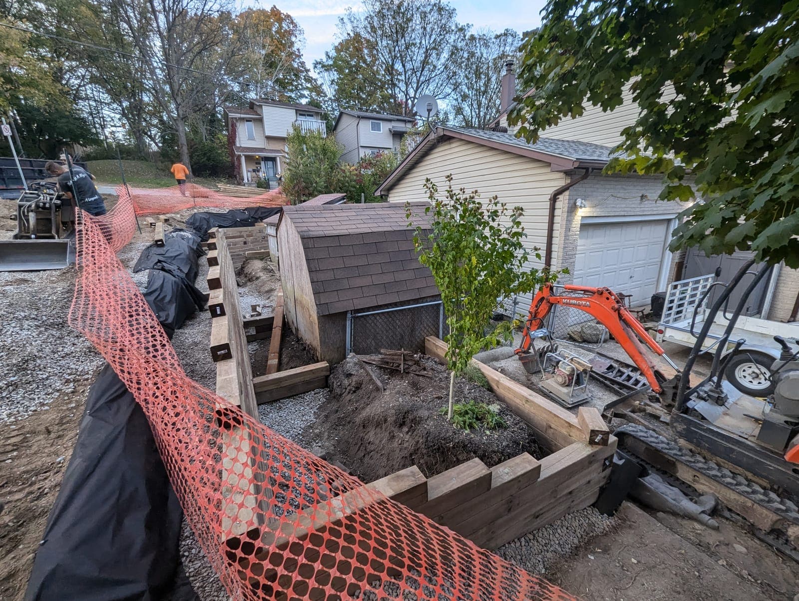 Timber retaining wall being installed with an excavator on a sloped backyard