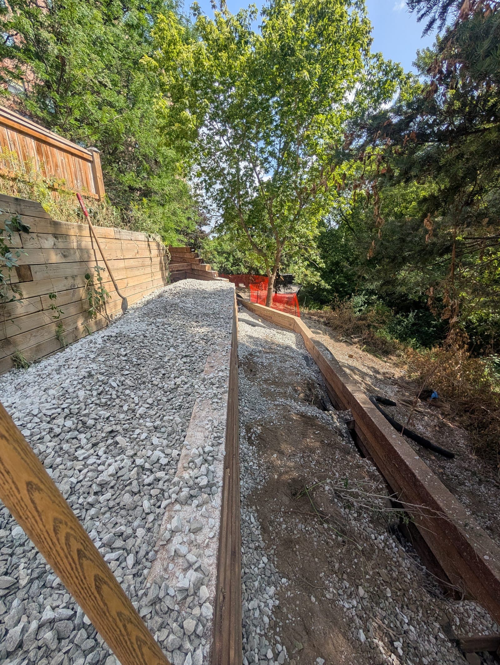 Timber retaining wall with integrated steps beside a fresh gravel pathway in a wooded backyard