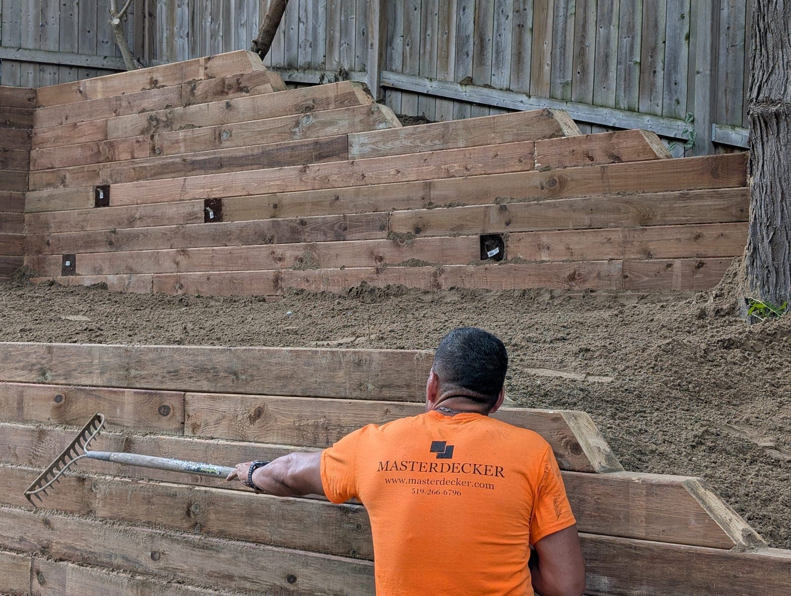Terraced timber retaining wall with integrated step lighting being backfilled in a backyard