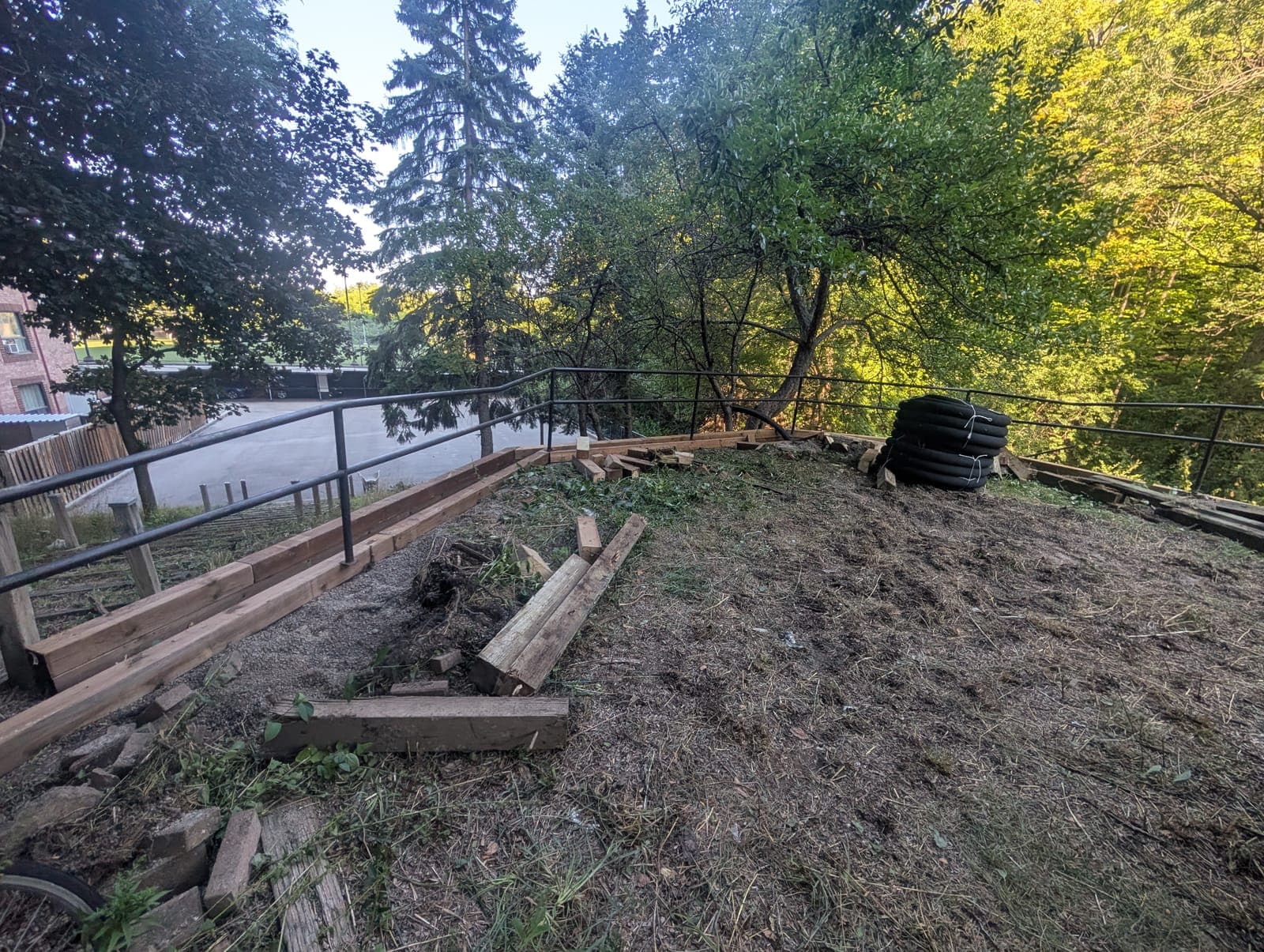 Timber retaining wall with safety railing along a hillside above a parking lot