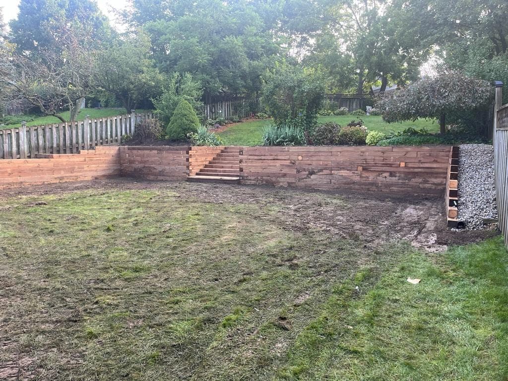 Timber retaining wall with integrated steps and a gravel drainage strip along the fence