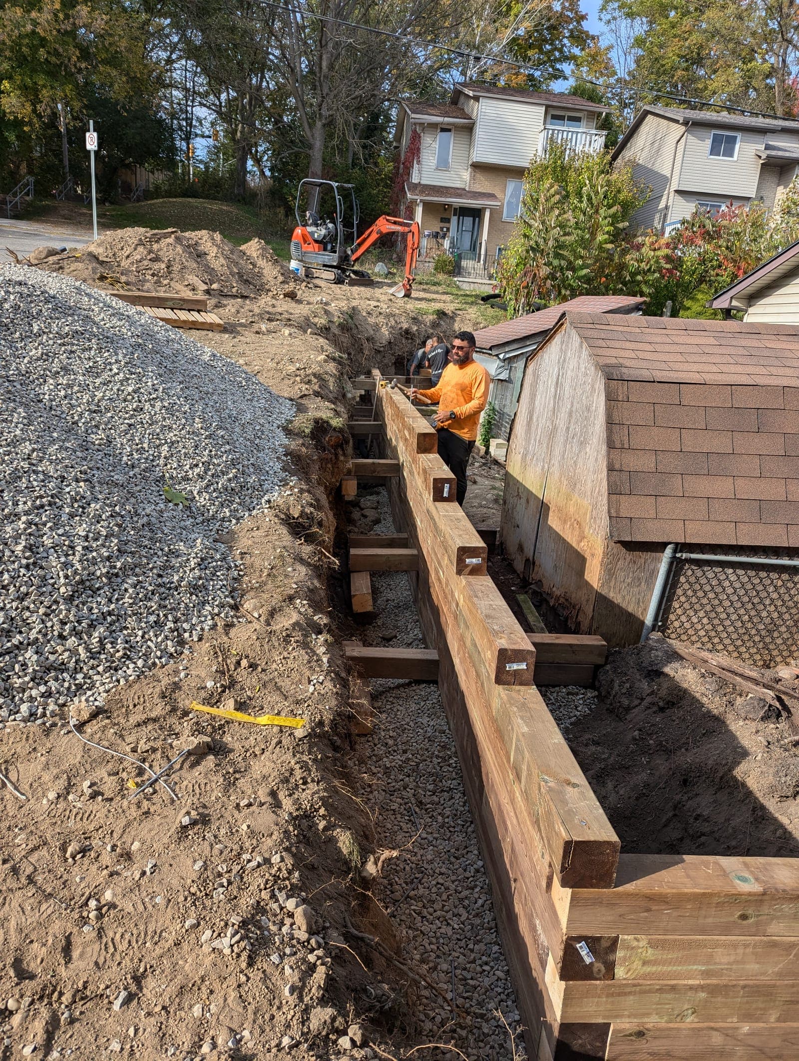 Large timber retaining wall being built with drainage gravel along a sloped yard