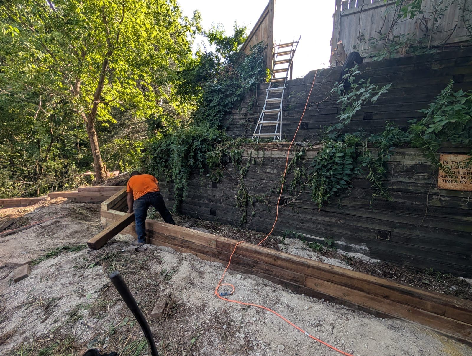 Contractor constructing a wood timber tie retaining wall along a steep landscaped slope