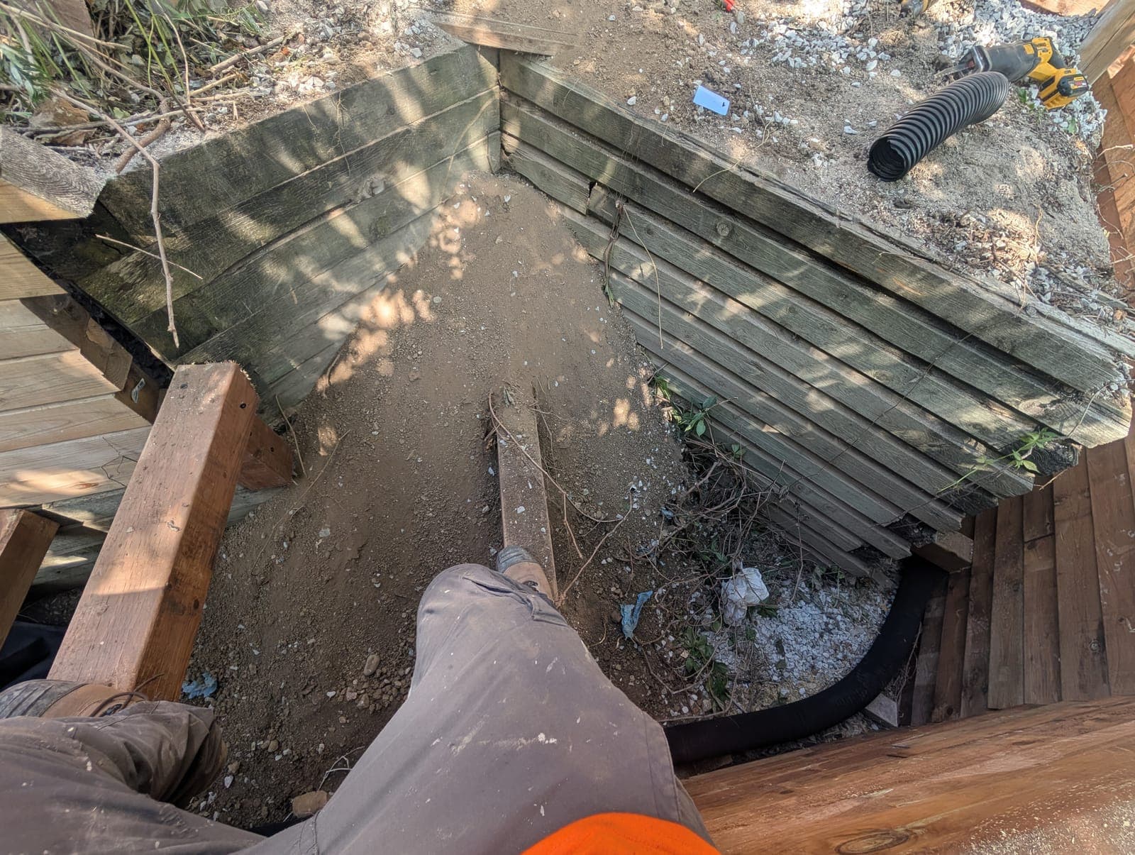 Weathered timber retaining wall corner being rebuilt with new drainage on a graded slope